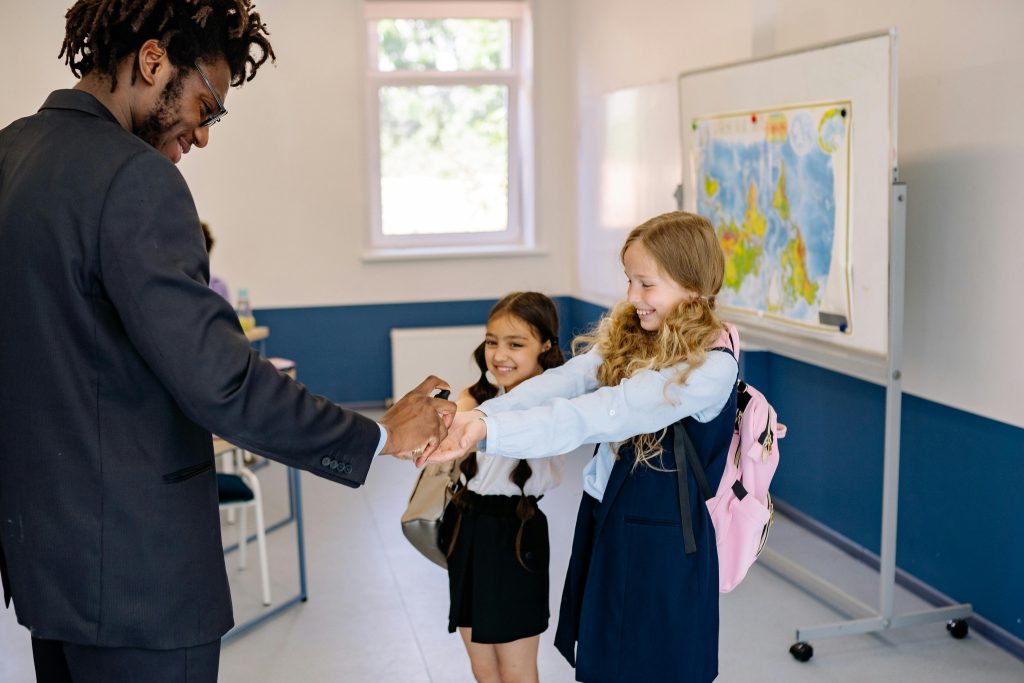 A teacher sanitizing two young students' hands in a classroom setting, promoting hygiene.